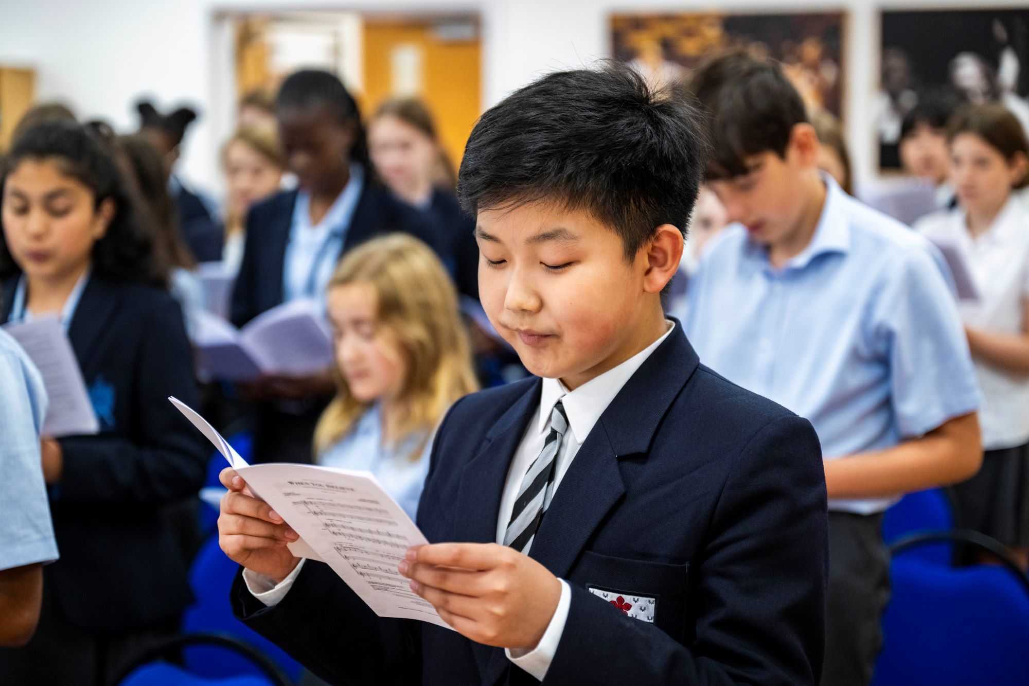 A male Alleyn's pupil looks at a music score during choir practice. Other pupils can be seen in the rows behind him.